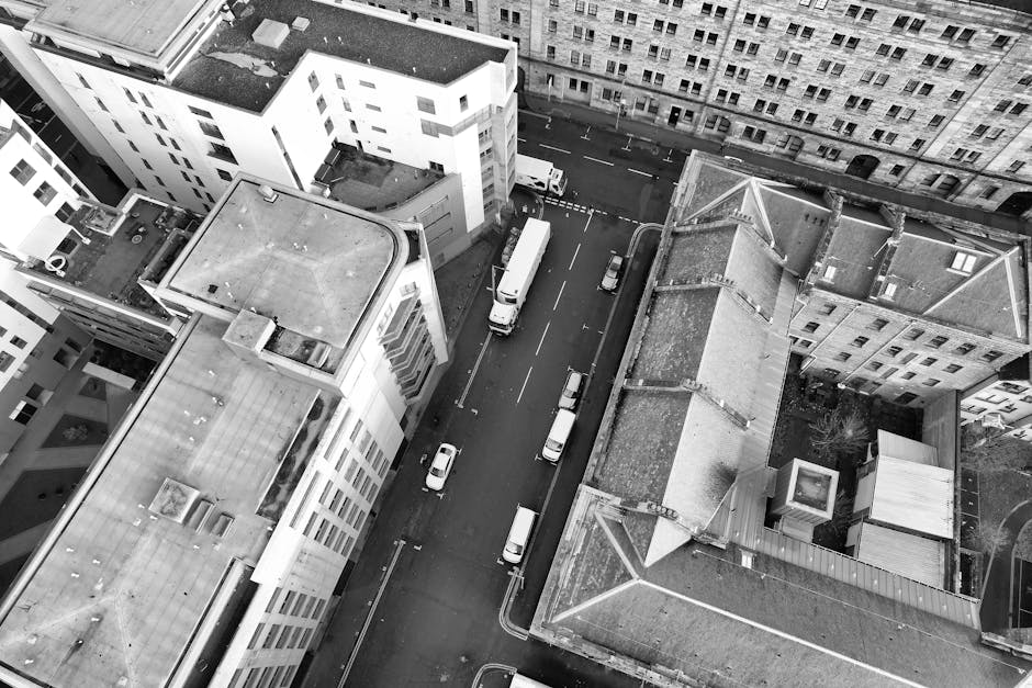 An aerial black-and-white photograph showing a narrow street surrounded by multi-storey residential buildings in Finchley, where house removals are underway by Removal Companies Finchley. The street f